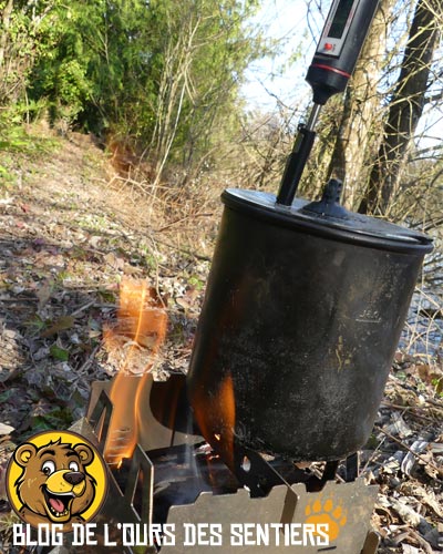 Remontée de flammes autour de la popote sur réchaud à bois en bivouac.